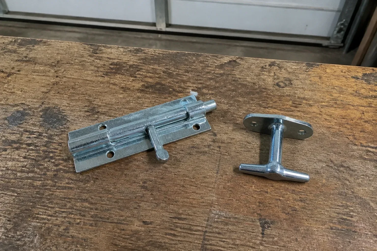 Detached slide bolt and T-handle on a wooden garage workbench. — Garage Door Manual Lock Repair, Markham