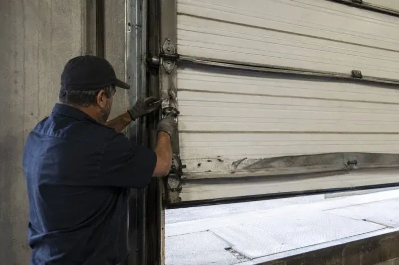 Person holding tools at the side hinge of a partly raised industrial sectional door — Commercial Sectional Door Repair, Markham