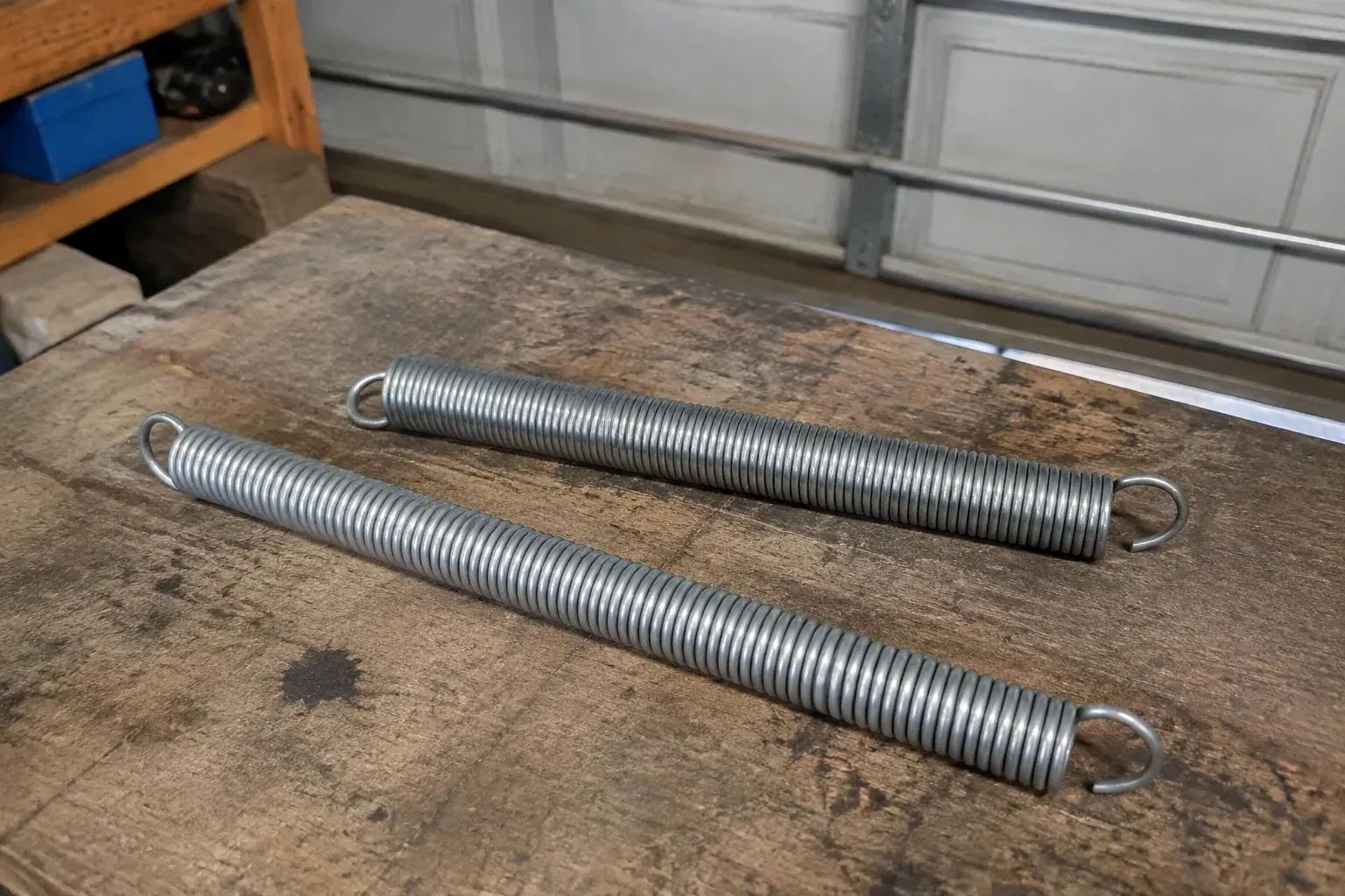 Two detached extension springs with hooked ends on a garage bench. — Extension Spring Replacement, Markham